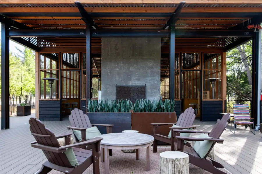 Covered concrete patio with a timber pergola, stone fireplace and Adirondack chairs