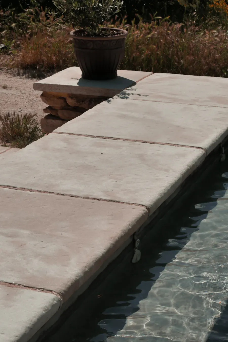 Concrete pool deck slabs and coping running along the edge of a swimming pool