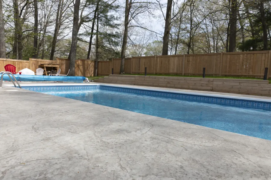 In-ground swimming pool with a broad stamped concrete deck and a timber privacy fence